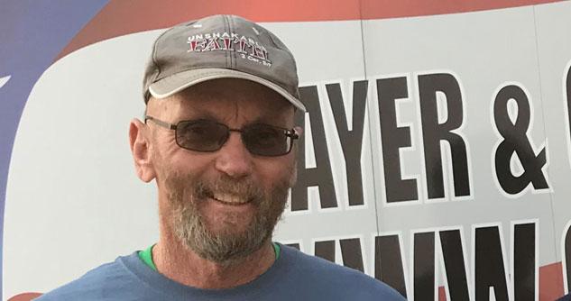 Man in a ball cap with shaded sunglasses and beard while smiling