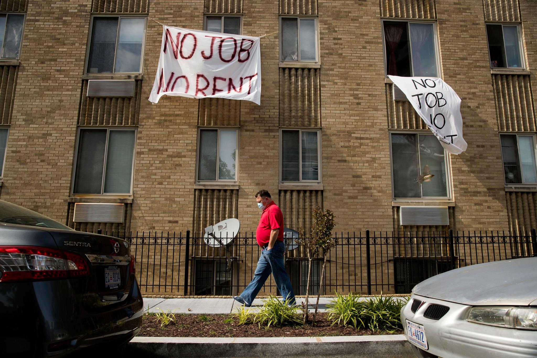 signs that read "No Job No Rent" hang from the windows of an apartment building