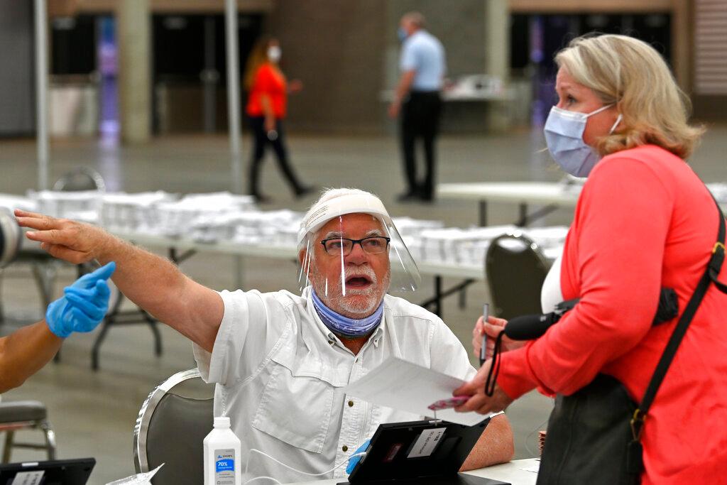 In this Tuesday, June 23, 2020 file photo, poll workers instruct a voter on where to go to fill out their ballot during the Kentucky primary at the Kentucky Exposition Center in Louisville, Ky. There was only one polling place open on election day this week in Louisville, Kentucky, and voting went relatively smoothly compared to other recent primaries amid the global pandemic. Does that mean other cities should consider the same in November? 