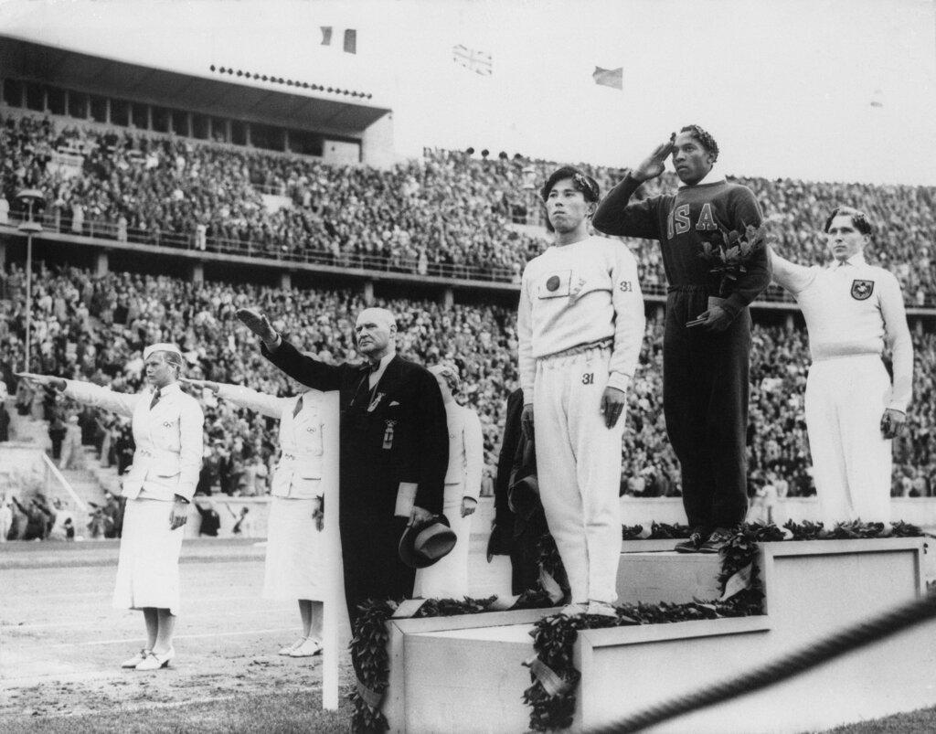 America's Jesse Owens, second from right, salutes during the presentation of his gold medal for the long jump, after defeating Nazi Germany's Lutz Long