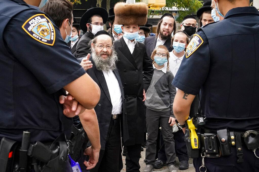 Members of the Orthodox Jewish community speak with NYPD officers on a street corner