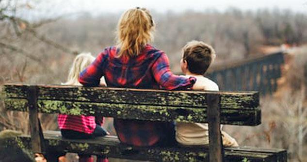 Mom, 2 kids, backs to us, sit on bench in nature
