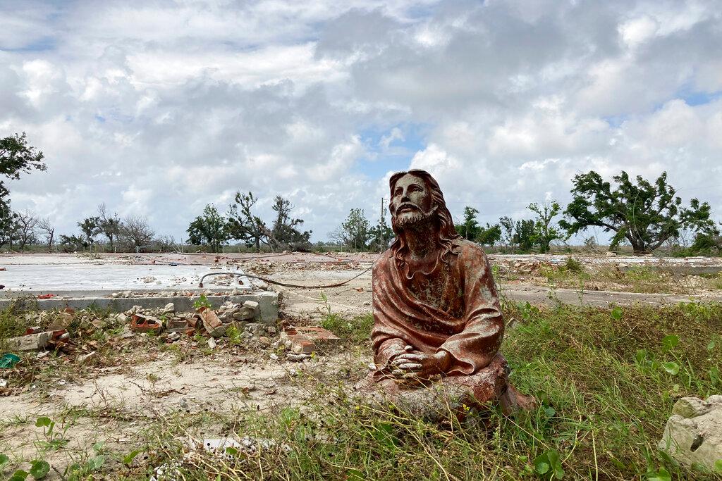 A statue of Jesus Christ stands in front of the remains of a house in Cameron Parish, La