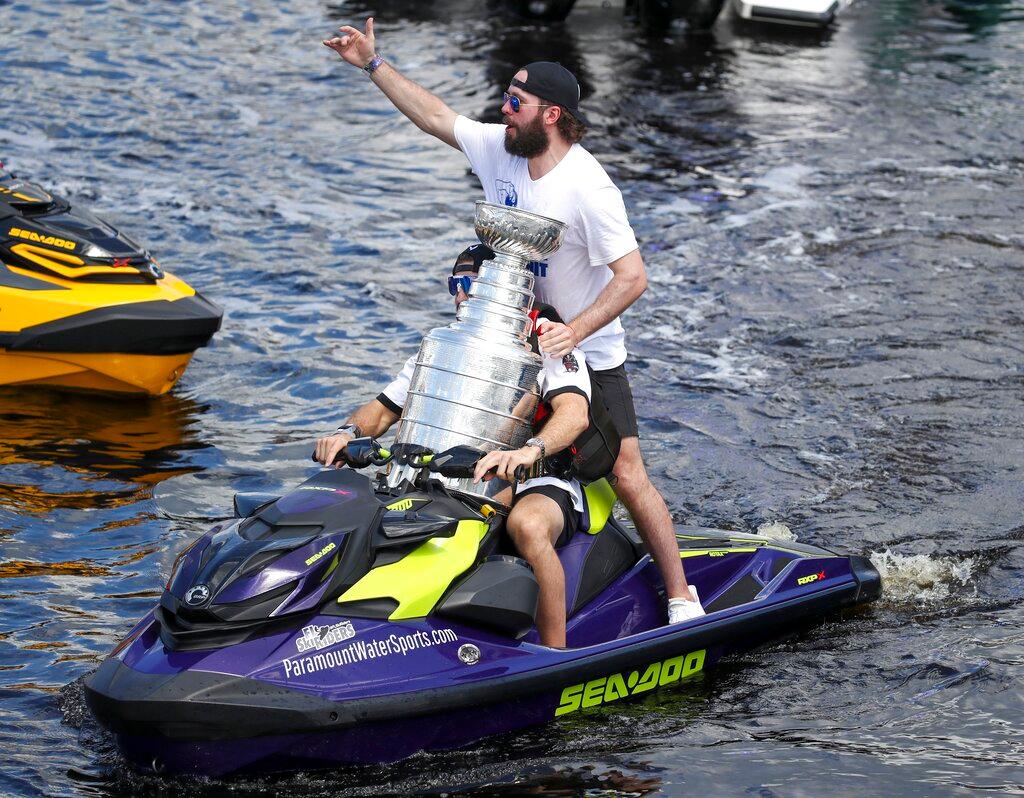 Tampa Bay Lightning left wing Alex Killorn drives a jet ski while holding the Stanley Cup as teammate Nikita Kucherov gestures to the crowd