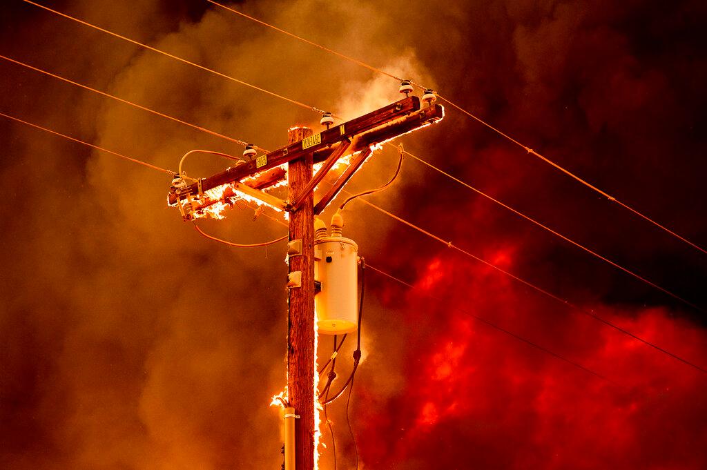 Fire burns along a power pole as the Sugar Fire, part of the Beckwourth Complex Fire, tears through central Doyle, Calif.