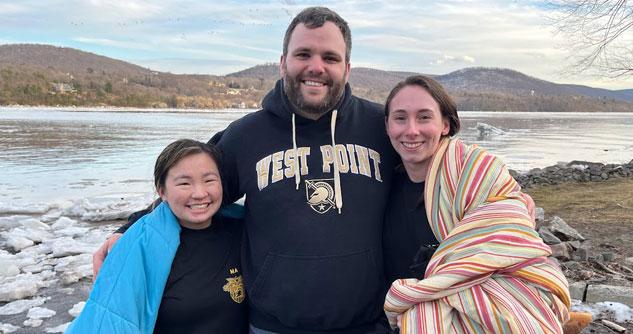 Two young women bundled up next to a man in a West Point sweatshirt