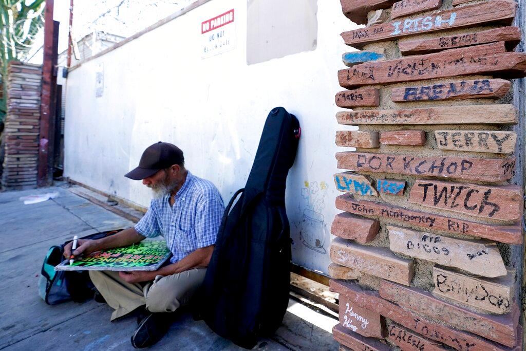 A homeless man works a sign as he sits next a monument to homeless people who have died  in Phoenix.