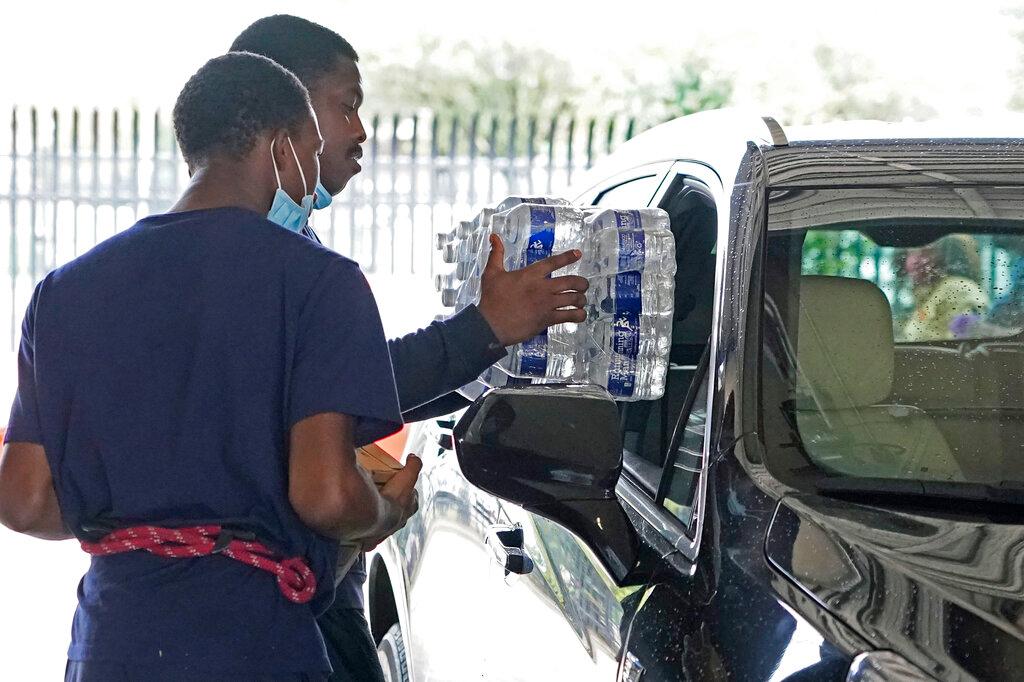 A recruit for the Jackson, Miss., Fire Department puts cases of bottled water in a resident's truck