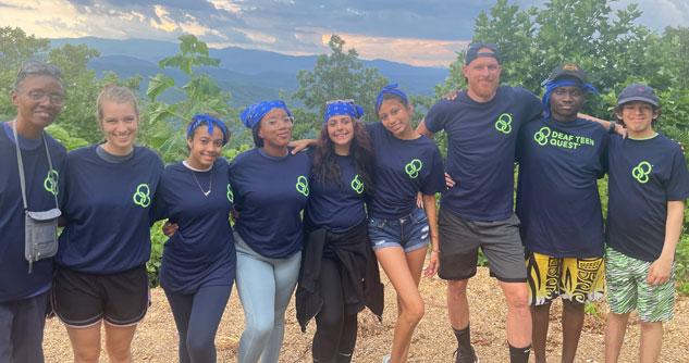 Nine people in blue t-shirts with mountains in the background