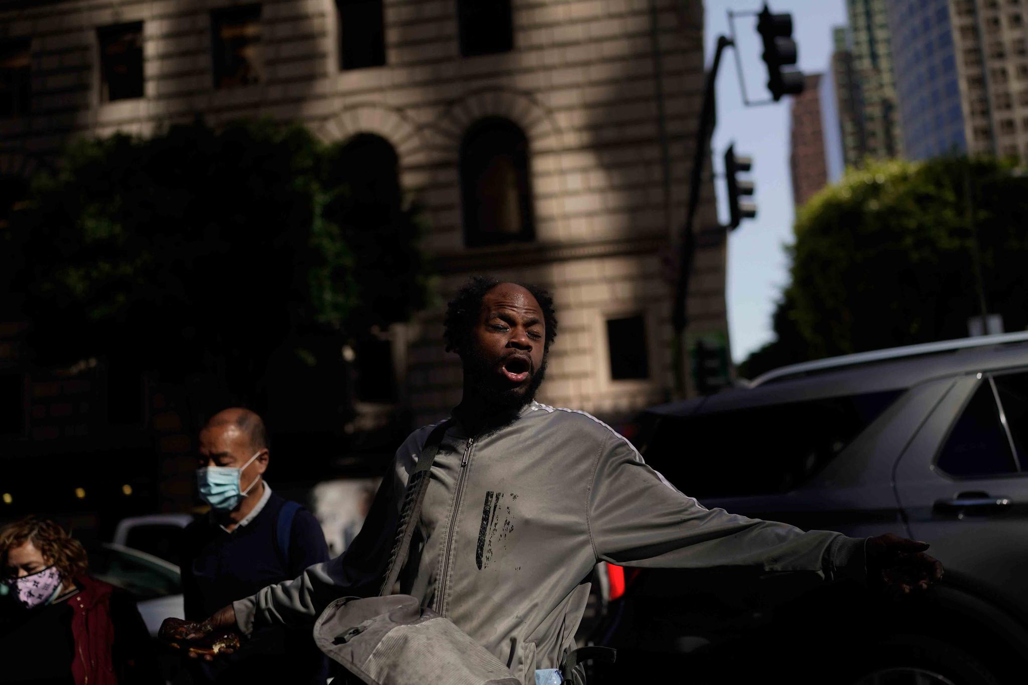 A mentally-ill homeless man talks aloud to himself as pedestrians walk across the street in downtown Los Angeles, Thursday, April 14, 2022.