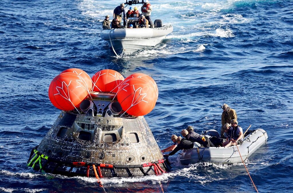 U.S. Navy divers secure NASA's Orion capsule during recovery operations after it splashed down in the Pacific.