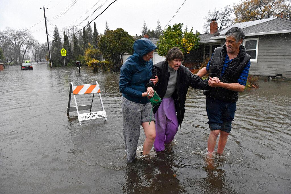 Nurse Katie Leonard, left, assists Scott Mathers, right, as they rescue Mathers' mother, Patsy Costello, 88, after being trapped in her vehicle for over an hour in California floodwaters