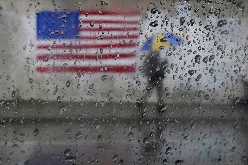 A pedestrian carries an umbrella while walking past a painting of the American flag in San Francisco