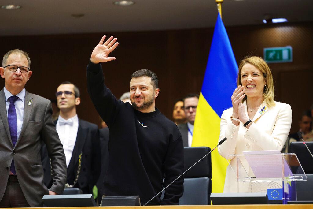 Ukraine's President Volodymyr Zelenskyy, center, gestures as European Parliament's President Roberta Metsola, right, applauds during an EU summit at the European Parliament in Brussels, Belgium