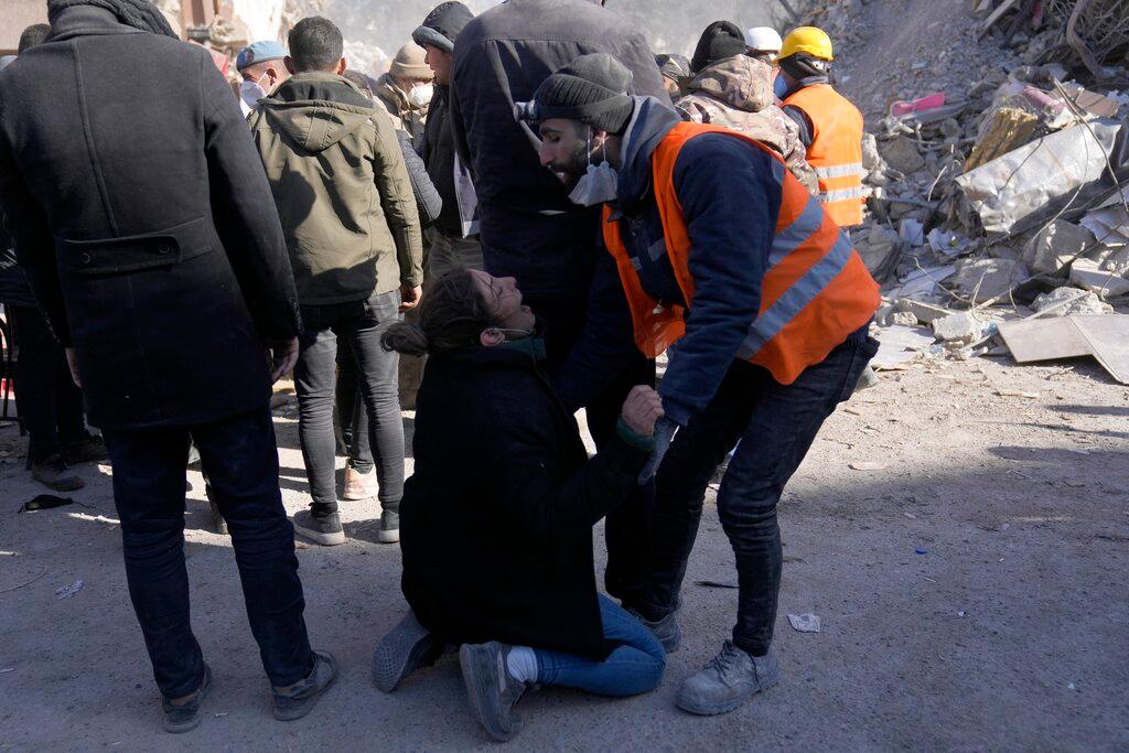 A woman is emotional as people stand in front of a destroyed building in Kahramanmaras, southeastern Turkey