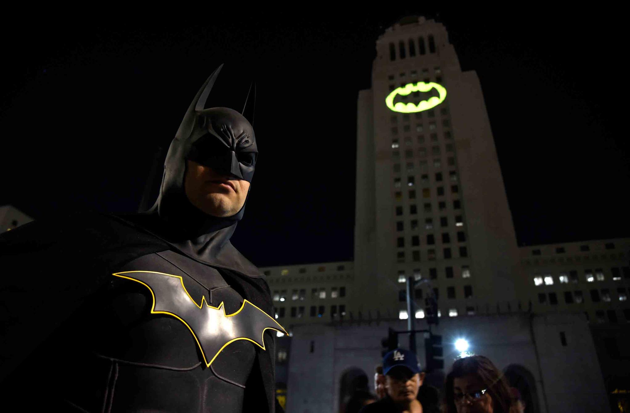 Tony Bradshaw, of Los Angeles, dressed as Batman, poses in front of a Bat-Signal projected onto City Hall during a tribute to "Batman" star Adam West