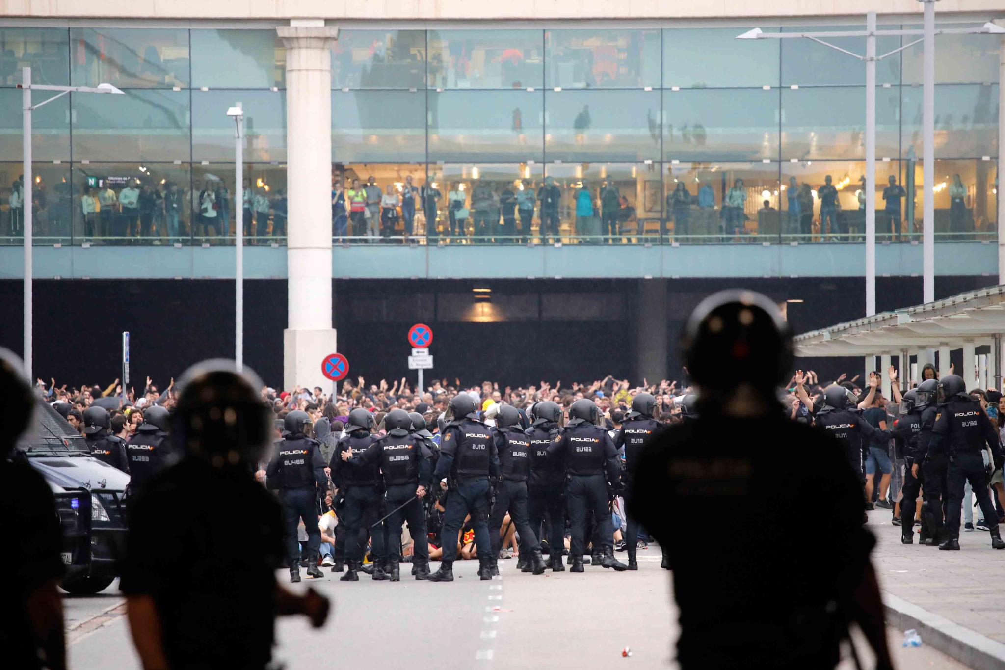 A line of riot police stands in front of protestors outside El Prat airport in Barcelona, Spain