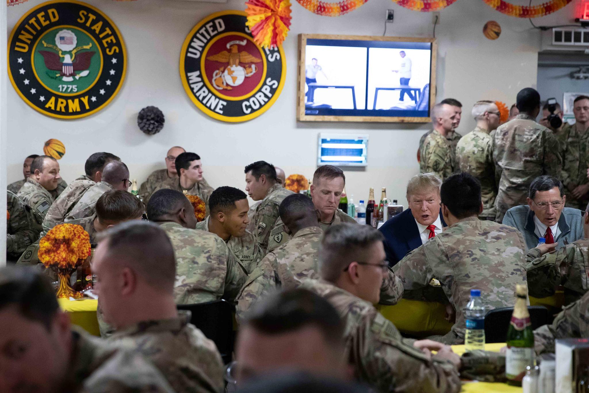 President Donald Trump, accompanied by Sen. John Barrasso, R-Wyo., right, sits down to have dinner with the troops during a surprise Thanksgiving Day visit