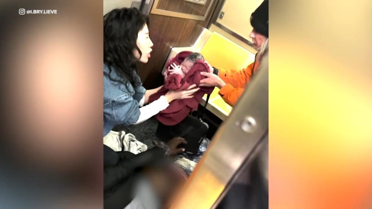 A woman holding a newborn baby in a subway train.